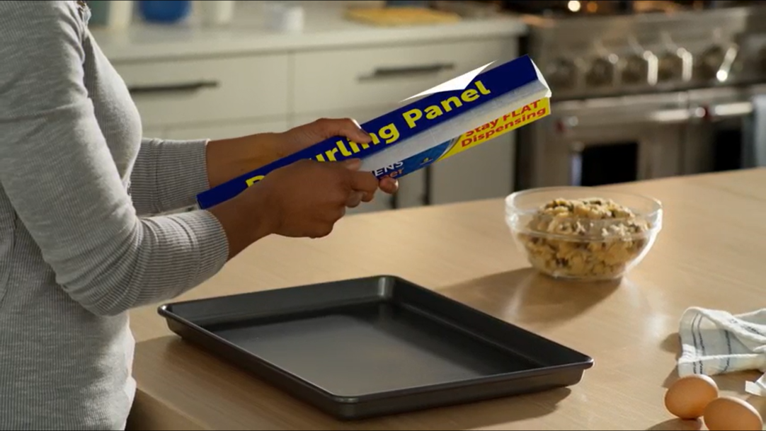 woman standing in a kitchen dispensing parchment paper for a pan